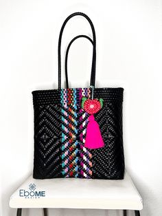 a black bag with a pink tassel on the handle and a red pom - pom hanging from it