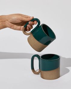 a person holding a green coffee mug in their left hand and another cup on the right