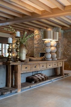 a large wooden table sitting in the middle of a living room next to a stone wall