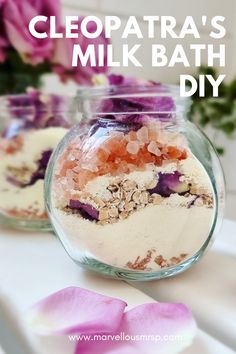 two jars filled with different types of bath salts on top of a white table next to pink flowers