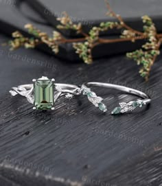 two rings with green stones and leaves on top of a wooden table next to a twig