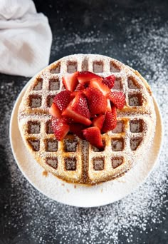 a waffle covered in powdered sugar and topped with strawberries on a plate