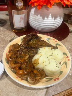 a plate with meat, mashed potatoes and gravy next to a bottle of booze