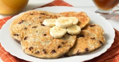 pancakes with banana slices and raisins on a plate next to a glass of orange juice