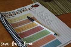 an open notebook sitting on top of a wooden table next to a pen and paper