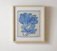 a blue and white flower is in a wooden frame on the wall next to a shelf