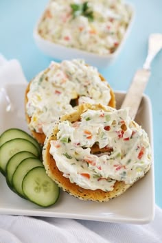 two bagels with cream cheese and cucumbers on a plate