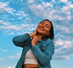 a woman standing in front of a blue sky with white clouds and smiling at the camera