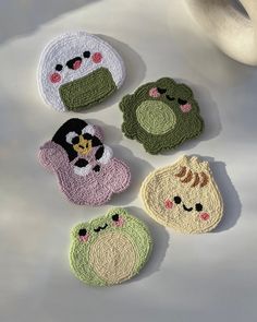 four crocheted animal coasters sitting on top of a white table next to a cup