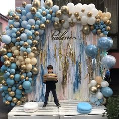 a young boy is standing in front of a backdrop made out of balloons and streamers