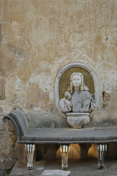 a stone bench sitting next to a wall with a statue on it's back