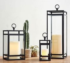 two black lanterns sitting on top of a wooden table next to a cacti