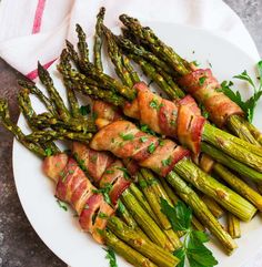 asparagus wrapped in bacon on a white plate with parsley garnish