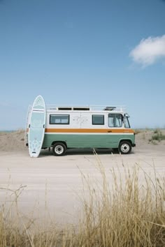 an old van with a surfboard on the back parked in front of some tall grass