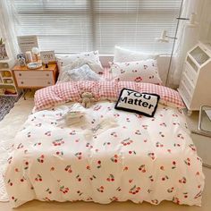 a bed with white sheets and red checkered pillow cases on it, next to a window