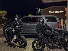 two motorcycle riders wearing skeleton face paint sit in front of a gas station at night