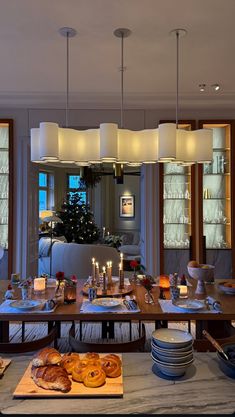 a dining room table is set with plates and bowls, candles, and breads