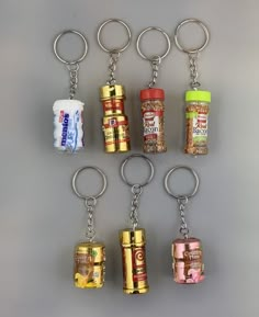 six key chains with different types of food in them on a gray surface, one has a bag of chips and the other is an empty can