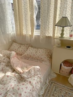 a bed sitting under a window next to a lamp on a table in front of a window