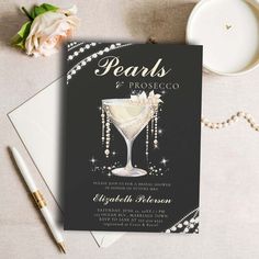 a black and white wedding card with pearls on the front, and a champagne glass in the middle