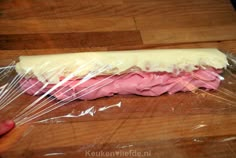 a piece of food wrapped in plastic sitting on top of a wooden table next to a person's hand