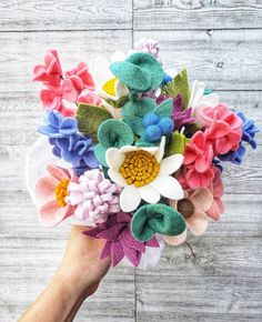 a woman's hand holding a bouquet of colorful flowers on top of a wooden table