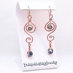 the earrings are made with copper wire and blue glass beads, on top of a white stand