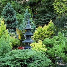 a stone lantern in the middle of a garden filled with trees and shrubs, surrounded by evergreens