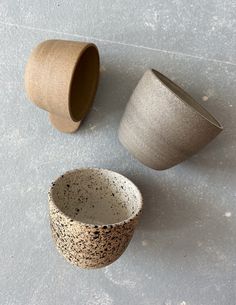 three ceramic cups sitting on top of a white floor next to each other and one cup with black speckles