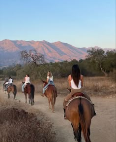 four people are riding horses on a dirt path in front of some hills and trees