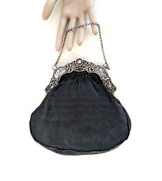 A black handbag with a Dutch 2nd standard silver (.833 purity), repousse frame with windmills, birds, a baby's face, and a cable chain handle.  The interior of the bag is hand sewn, taupe thick gauge, silk satin, and it has two small, side pockets.  The exterior silk is a finely ribbed matte black silk.  The handle drop is 3 1/2 inches, its overall dimensions are 7 1/2 H x 7 1/2 W x 1/2 D inches.  The bag dates from the late 19th to the first half of the 20th century. CONDITION:  Some signs of w Silver Handheld Evening Bag With Chain Strap, Handheld Silver Evening Bag With Chain Strap, Elegant Silver Bag With Chain Strap, Luxury Silver Evening Bag With Detachable Handle, Silver Formal Bag With Chain Strap, Handheld Evening Bag With Silver-tone Hardware, Silver Shoulder Bag With Palladium Hardware For Evening, Elegant Engraved Shoulder Bag, Elegant Silver Shoulder Bag As Gift