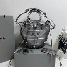 Balenciaga 's popular 'Le Cagole' series is a modern interpretation of its 'City' handbags - reshaped into a bucket bag design to inject a new soul into it. The large size adds two round top handles, combining classic and Modern trends are perfectly integrated. On the basis of retaining the original DNA of the motorcycle bag's flat rivets, delicate buckles and tassel zippers, it adds adjustable woven shoulder straps and a cute and playful heart-shaped mirror, which perfectly softens the neutral New Soul, Dumpling Bag, Motorcycle Bag, Lv Purse, Lv Shoes, Makeup Party, Birkin Kelly, Happy Fashion, Gucci Bamboo