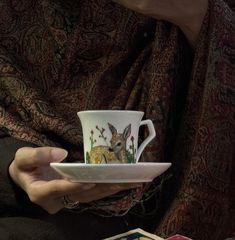 a person holding a cup and saucer with a deer painted on the inside of it