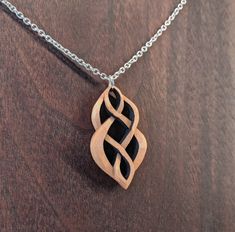 a wooden pendant is sitting on a table next to a silver chain that has an intertwined design