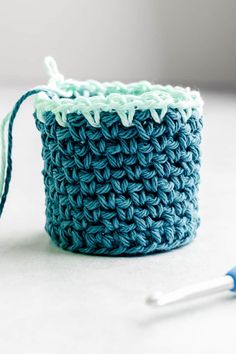 a crocheted blue and white basket sitting on top of a table next to a pair of scissors