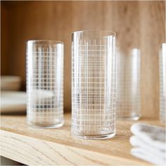 three clear glass cups sitting on top of a wooden table next to another glass cup