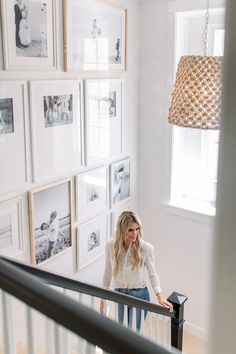 a woman standing on the stairs in front of many framed pictures and a chandelier