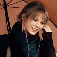 a woman is sitting under an umbrella talking on her cell phone and smiling at the camera