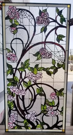 a stained glass window with pink flowers and green leaves on the outside, in front of a building