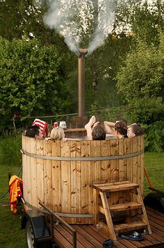 people relaxing in a wooden hot tub with steam coming from the top and on wheels