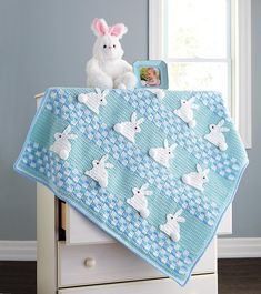 a crocheted blanket with white rabbits on it and a teddy bear next to it