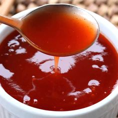 a spoon full of sauce being poured into a white bowl on top of a table