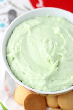 a white bowl filled with green frosting next to crackers on a paper plate