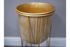 a gold planter sitting on top of a wooden floor next to a gray wall