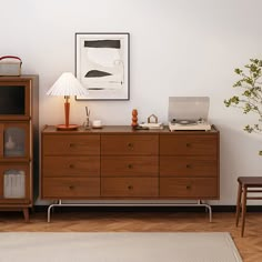 a room with a wooden dresser, lamp and pictures on the wall above it that has a white rug