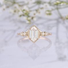 an emerald cut diamond ring on a white surface with some flowers in the back ground