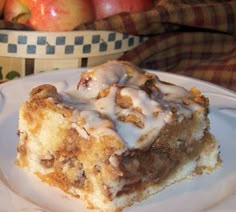 a piece of cinnamon roll cake on a white plate with apples in the back ground