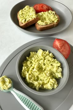 there are two plates with food on them and one plate has bread, tomato slices, and the other is avocado