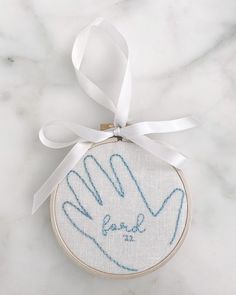 a hand embroidered onto a piece of cloth hanging from a white ribbon on a marble surface