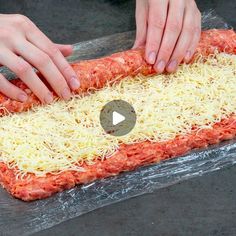 two hands are sprinkling cheese on top of an uncooked meatloaf